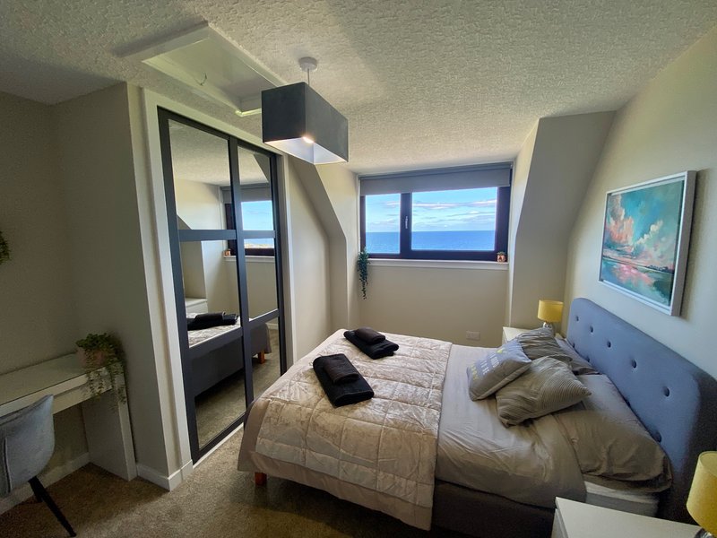 Bright bedroom with double bed, white bedside table, mirrored wardrobe and sea view window