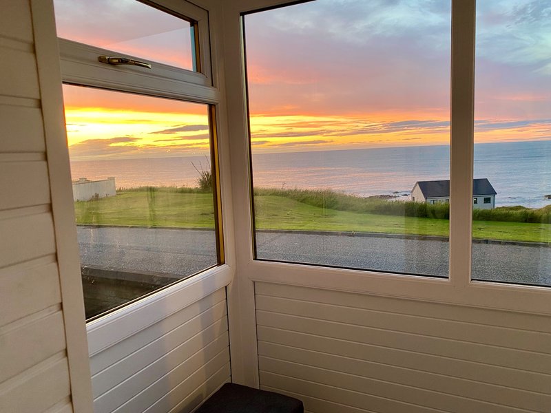 View through large windows of waterfront sunset, green fields, and distant houses