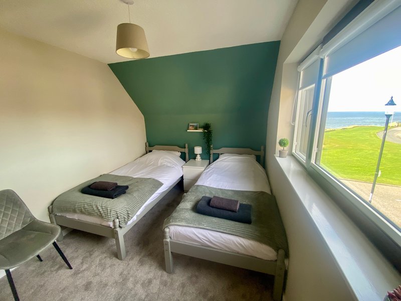 Twin bedroom with two single beds, green accent wall, pendant lamp and countryside view through windows
