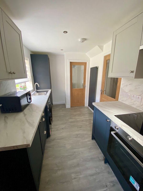 Modern galley kitchen with dark blue cabinetry, white countertops, stainless steel appliances and wooden doors