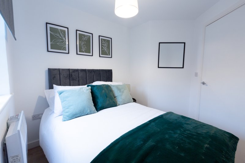 Modern bedroom with double bed, blue and teal pillows, dark headboard, framed prints