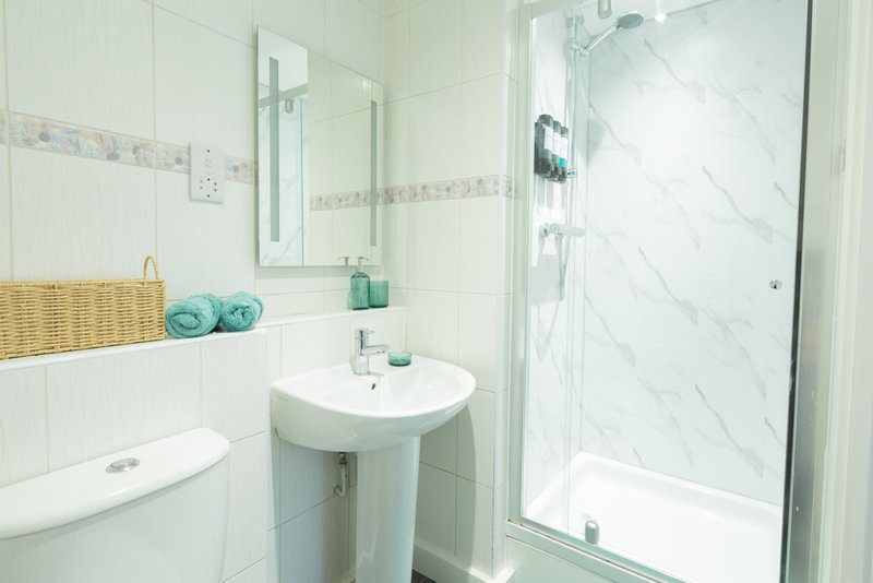 Clean modern bathroom with pedestal sink, shower enclosure, and turquoise towels
