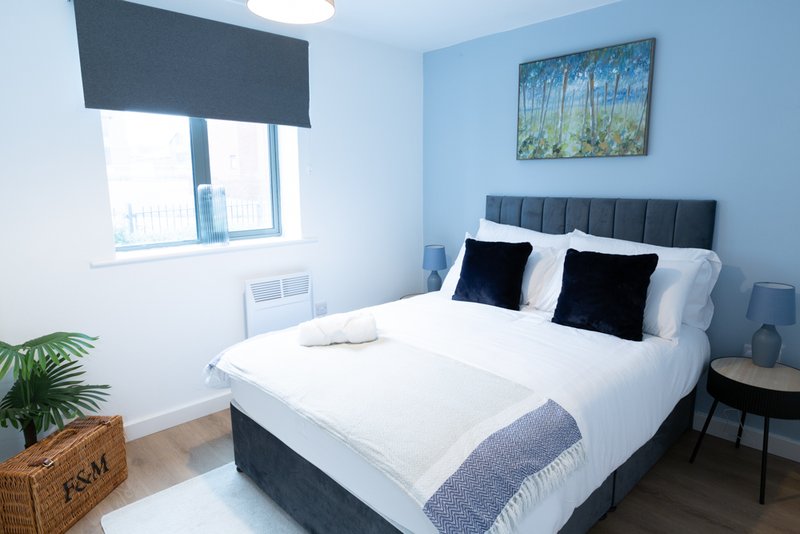 Modern bedroom with double bed, black headboard, white bedding, and blue accent wall