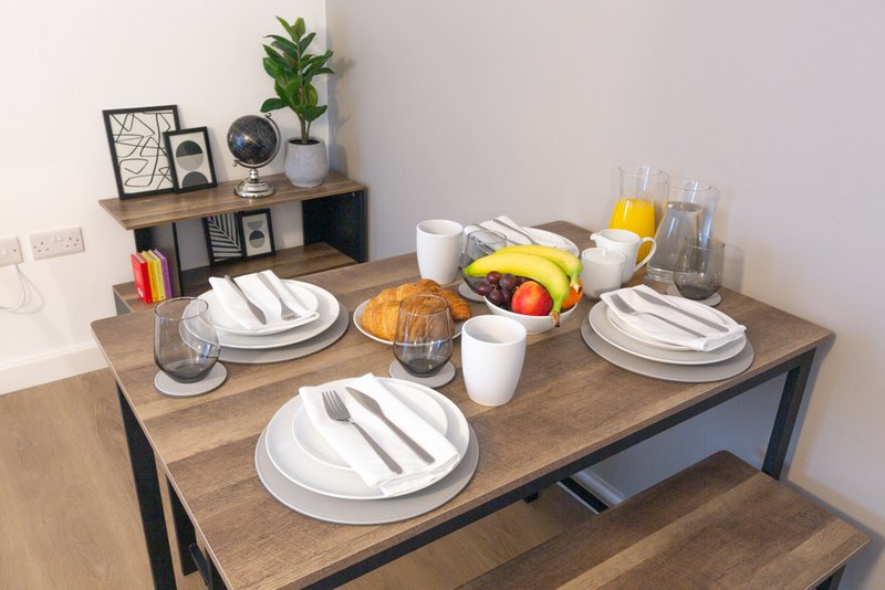 Dining table set for three with white plates, cutlery, glasses and fresh fruit basket