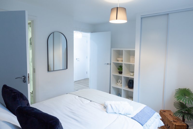 Bright modern bedroom with double bed, arched mirror, pendant light and built-in shelving