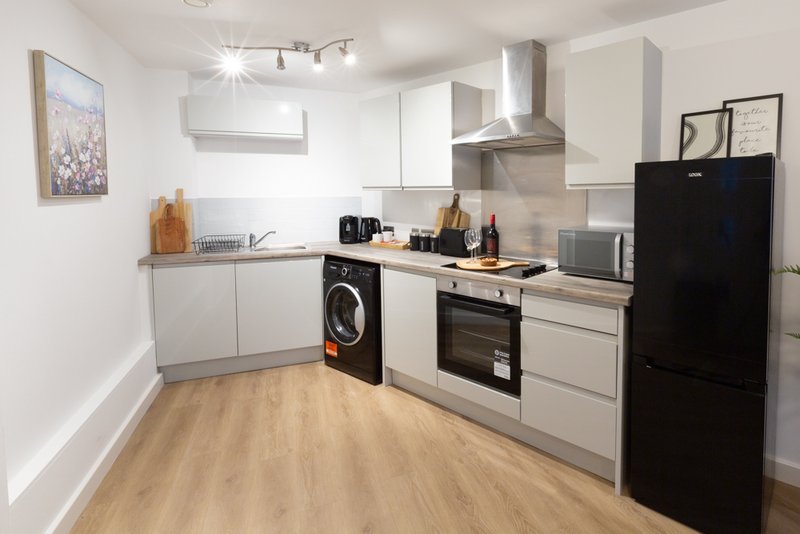Modern kitchen with white cabinetry, black appliances, wooden floor and stainless steel cooker hood
