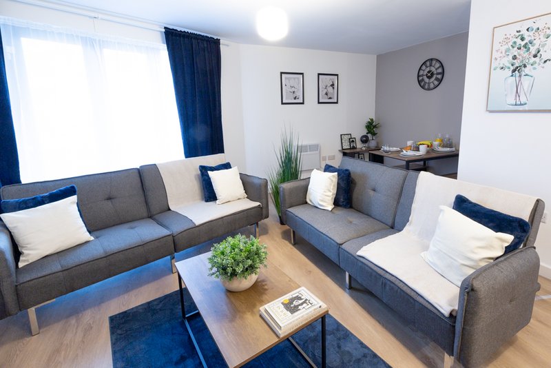 Modern living room with two gray sofas, potted plants, wooden coffee table and blue accents