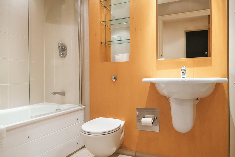 Modern bathroom with orange walls, white toilet, pedestal sink, mirror and shower enclosure