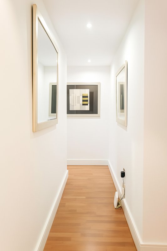 Long hallway with wooden floor, white walls, framed mirrors and artwork