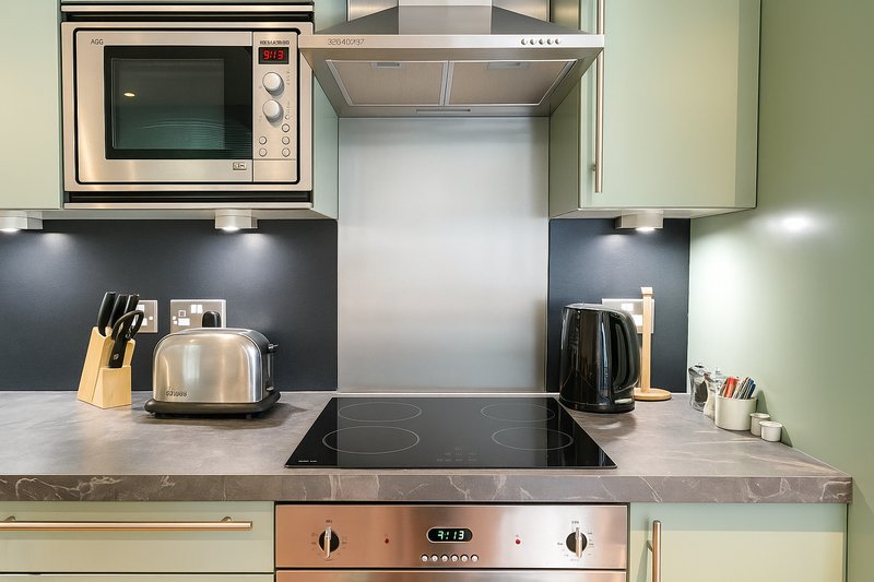 Modern kitchen with pale green cabinets, black backsplash, stainless steel appliances and countertop