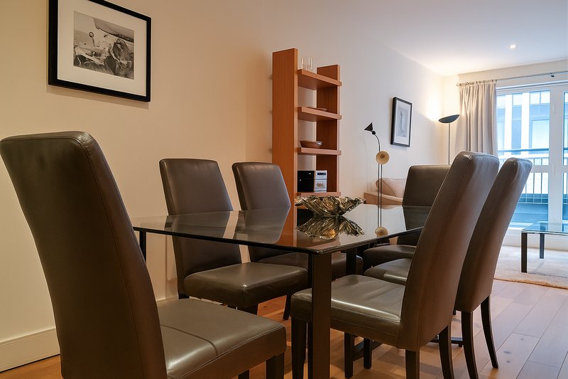 Modern dining room with black glass table, brown leather chairs, wooden shelving and ocean view through glass doors