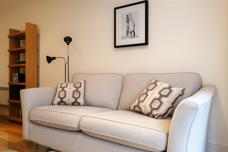 Living room with grey upholstered sofa, patterned cushions, wooden shelving unit and floor lamp