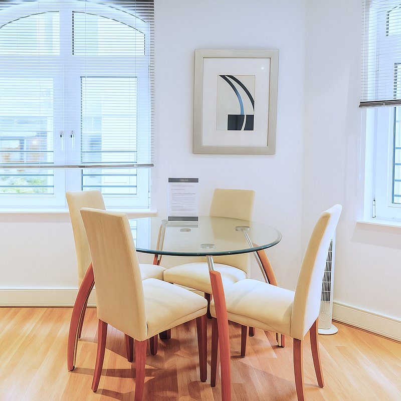 Modern dining area with round glass table, wooden chairs, and framed wall art