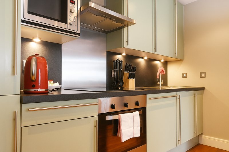 Modern kitchen with cream cabinets, black countertop, red kettle and integrated appliances