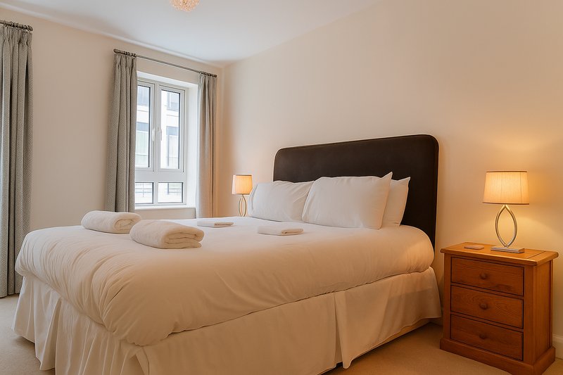 Bright bedroom with double bed, dark headboard, wooden nightstand and warm lighting