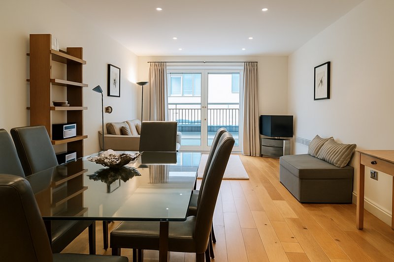 Open-plan living and dining room with wooden flooring, dining table, sofa, and glass doors to balcony