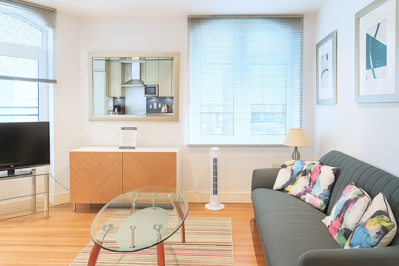 Modern living room with grey sofa, wooden furniture, round glass table and wall-mounted TV