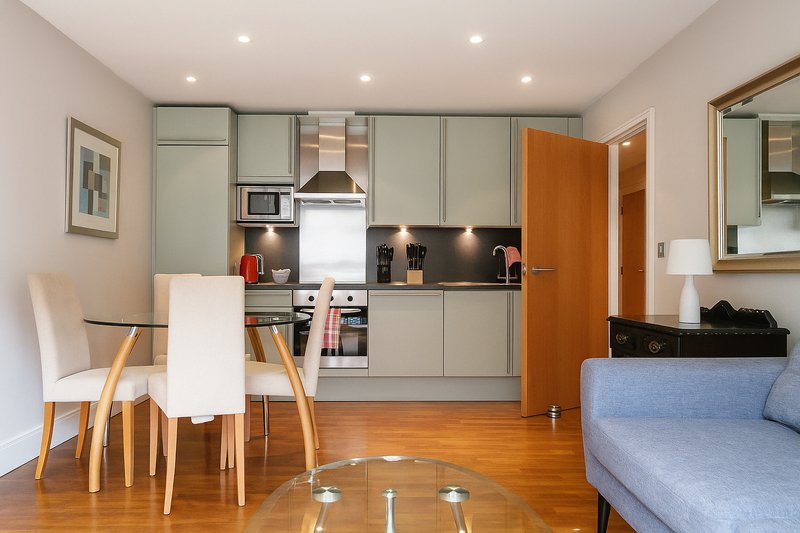 Open-plan kitchen and dining area with sage green cabinetry, wooden dining table, and sofa