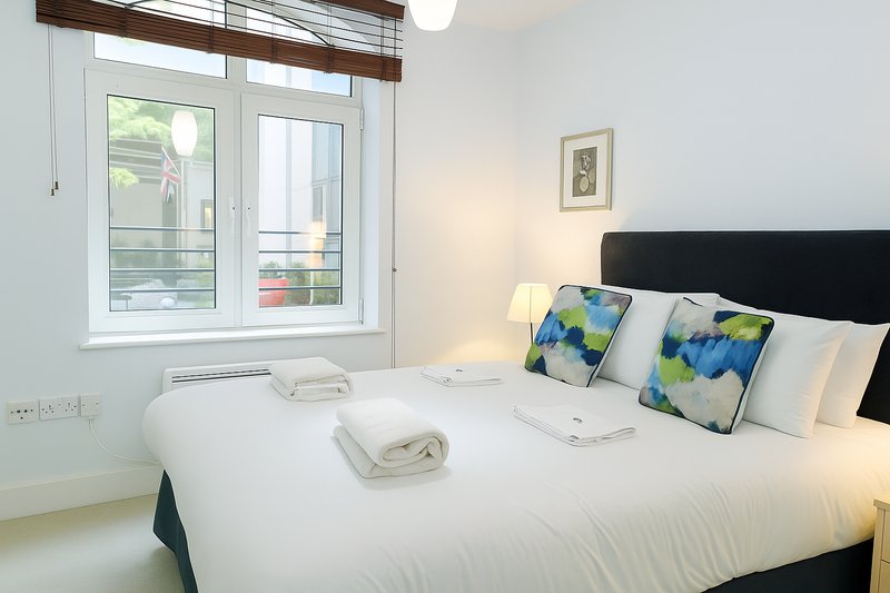 Modern bedroom with double bed, black headboard, colorful cushions and white bedding