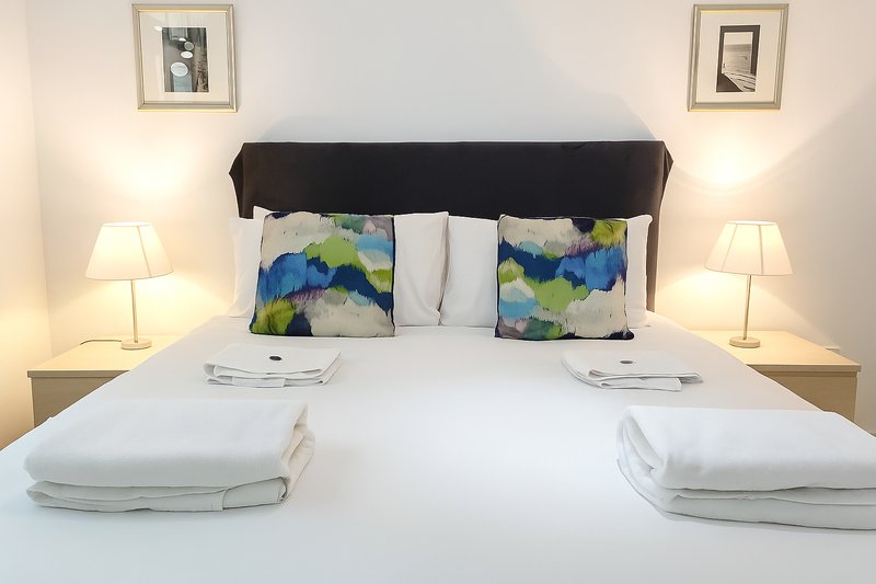Bright bedroom with double bed, colorful cushions, white bedding, twin lamps and framed wall art