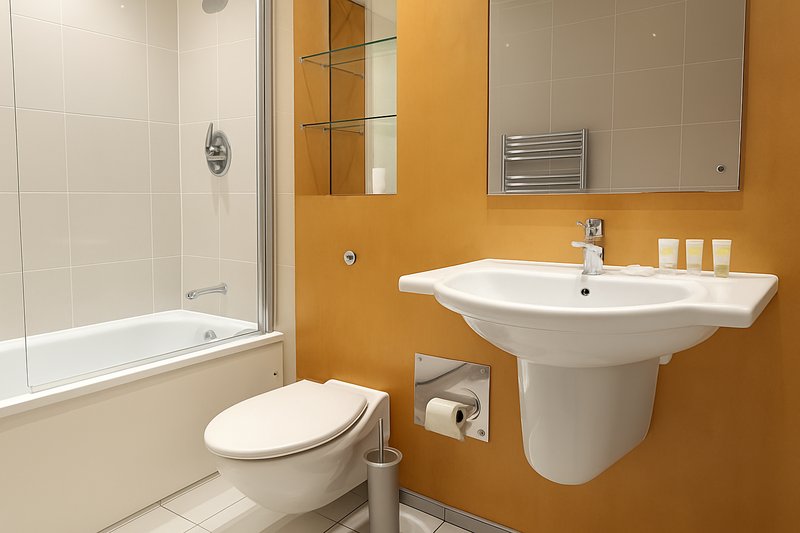 Modern bathroom with orange walls, white pedestal sink, toilet, and glass shower enclosure
