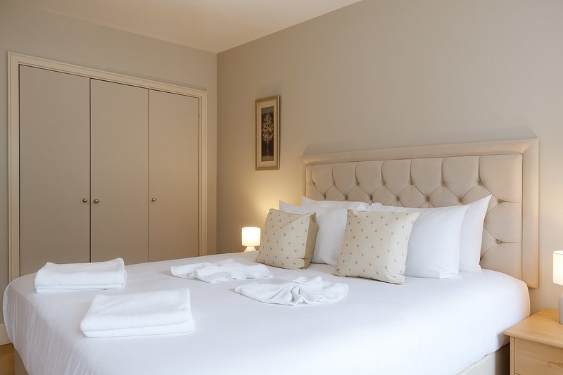 Bright bedroom with double bed, upholstered headboard, white bedding, pillows, and built-in wardrobe