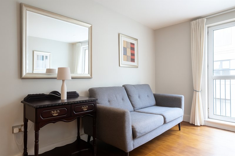 Modern living room with grey sofa, dark wooden desk, large mirror and balcony door