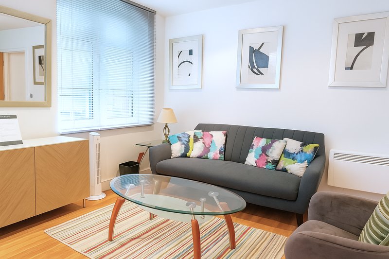 Modern living room with gray sofa, colorful cushions, glass coffee table, and framed wall art