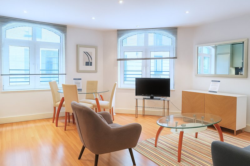Modern living room with armchair, dining table, TV, wooden floor and large windows