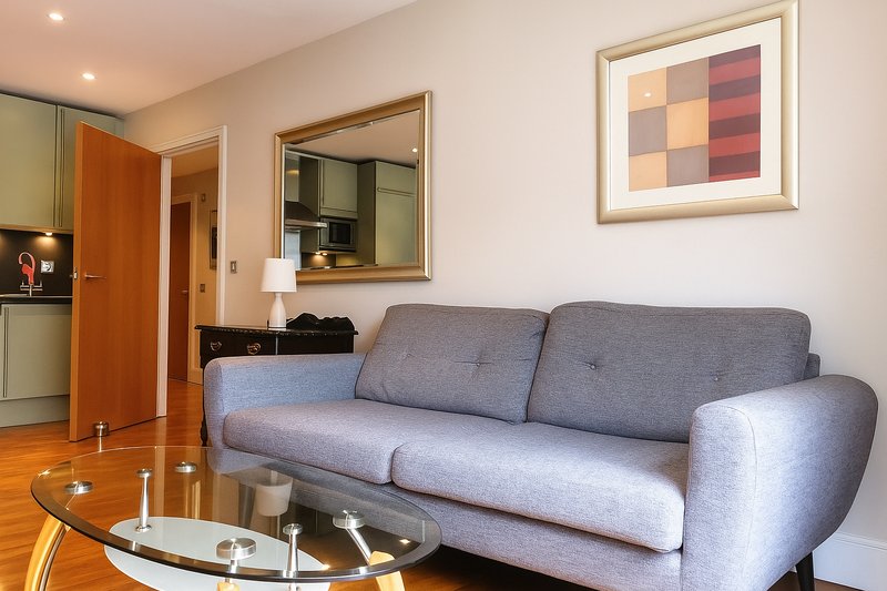 Modern living room with grey sofa, glass coffee table, wooden flooring and wall art