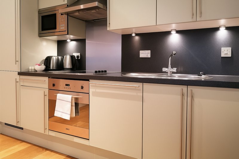 Modern kitchen with cream cabinets, black countertop, stainless steel appliances and under-cabinet lighting