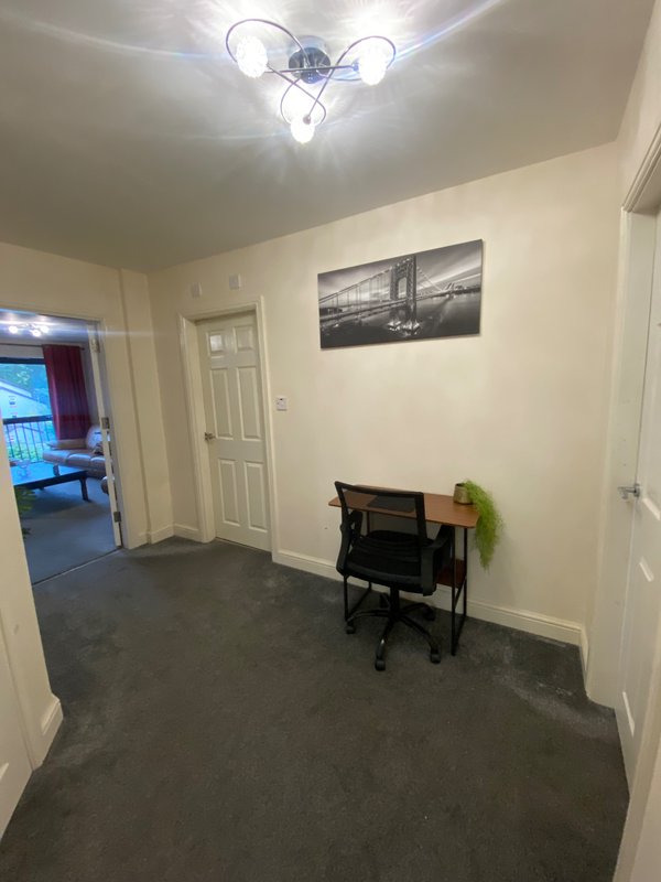 Hallway with ceiling light fixture, framed wall art, black piano, and potted plant