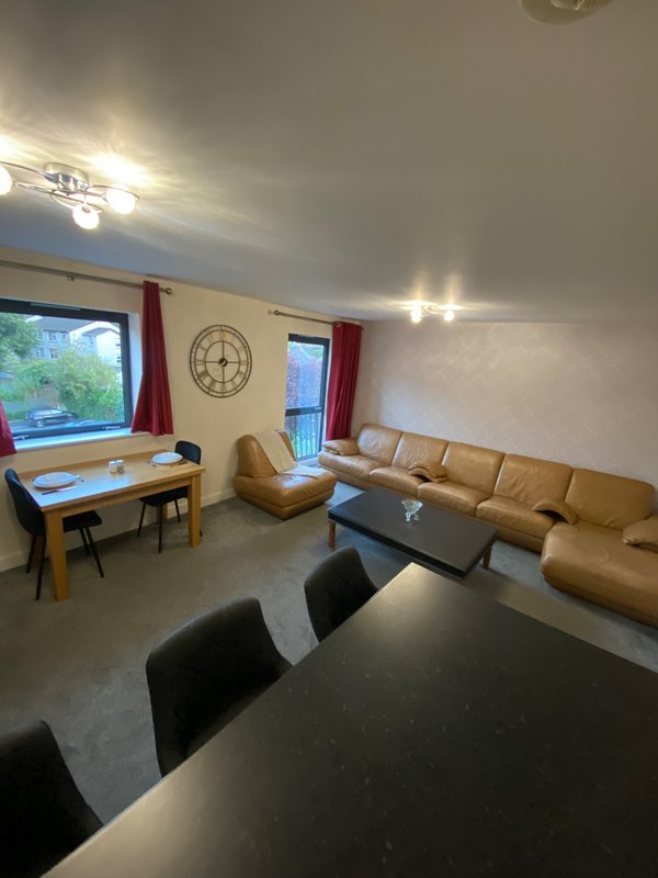 Open-plan living room with sofa, dining table, desk area and wall clock