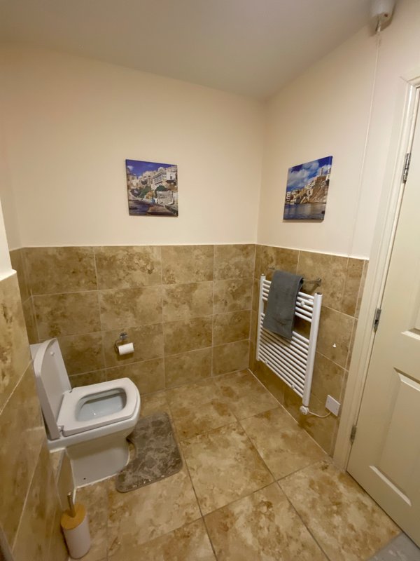 Bathroom with toilet, heated towel rail, tiled walls and floor, two framed prints