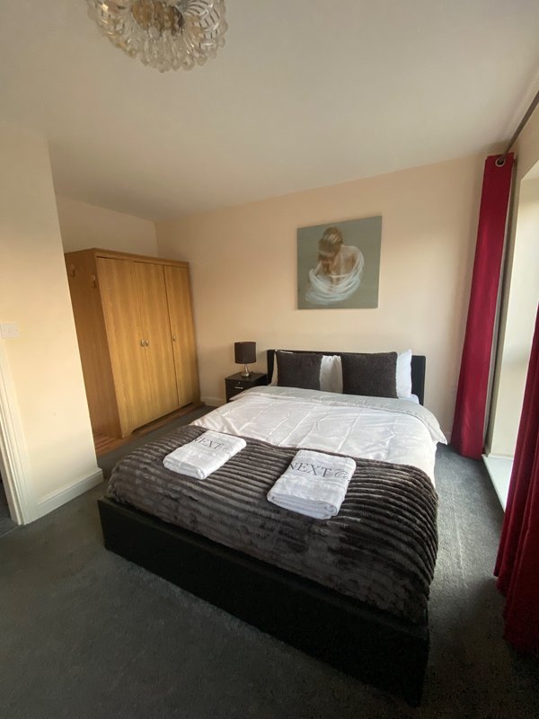 Bedroom with double bed, wooden wardrobe, framed wall art, and burgundy curtains