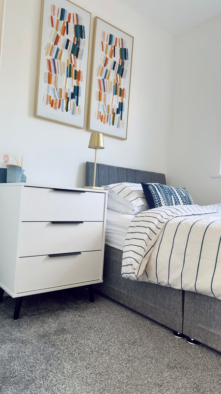 Modern bedroom with double bed, white bedside table, striped bedding and framed wall art