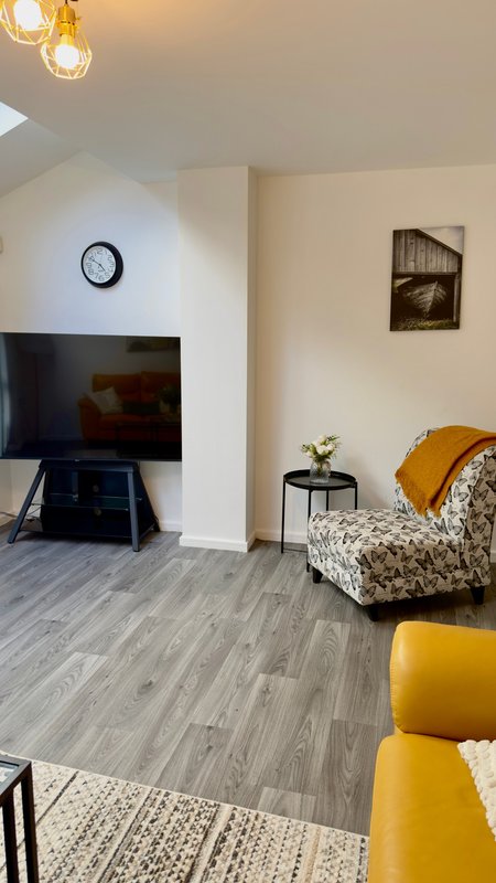 Open-plan living room with TV stand, patterned armchair, yellow ottoman, and pendant lighting