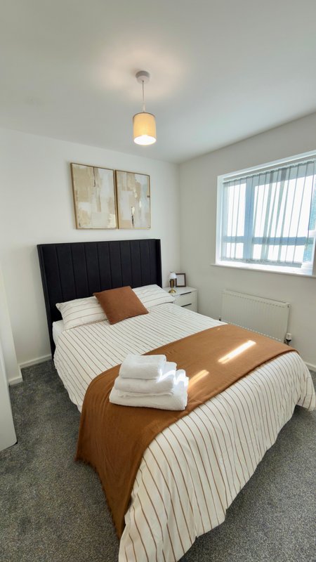Modern bedroom with black headboard, striped bedding, wooden bench, pendant light and window