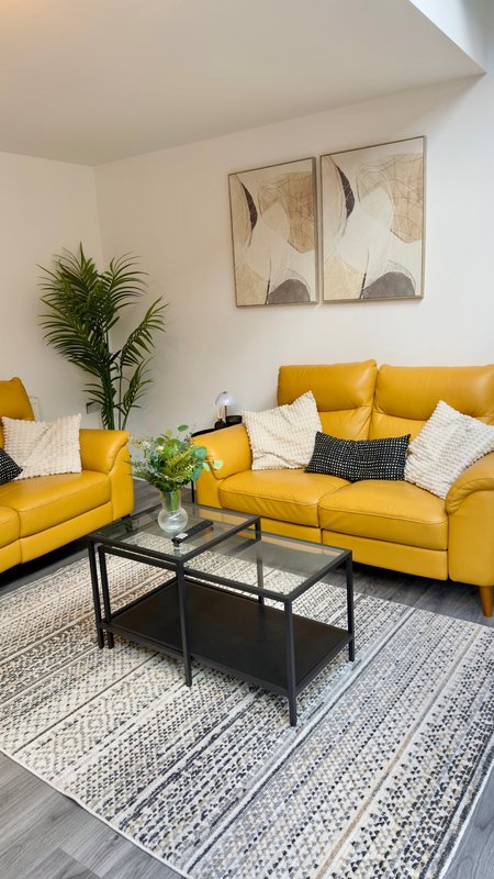 Modern living room with yellow sofas, black coffee table, potted plant and abstract wall art