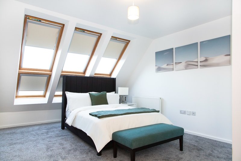 Bright attic bedroom with skylight windows, double bed, teal bench, and landscape wall art