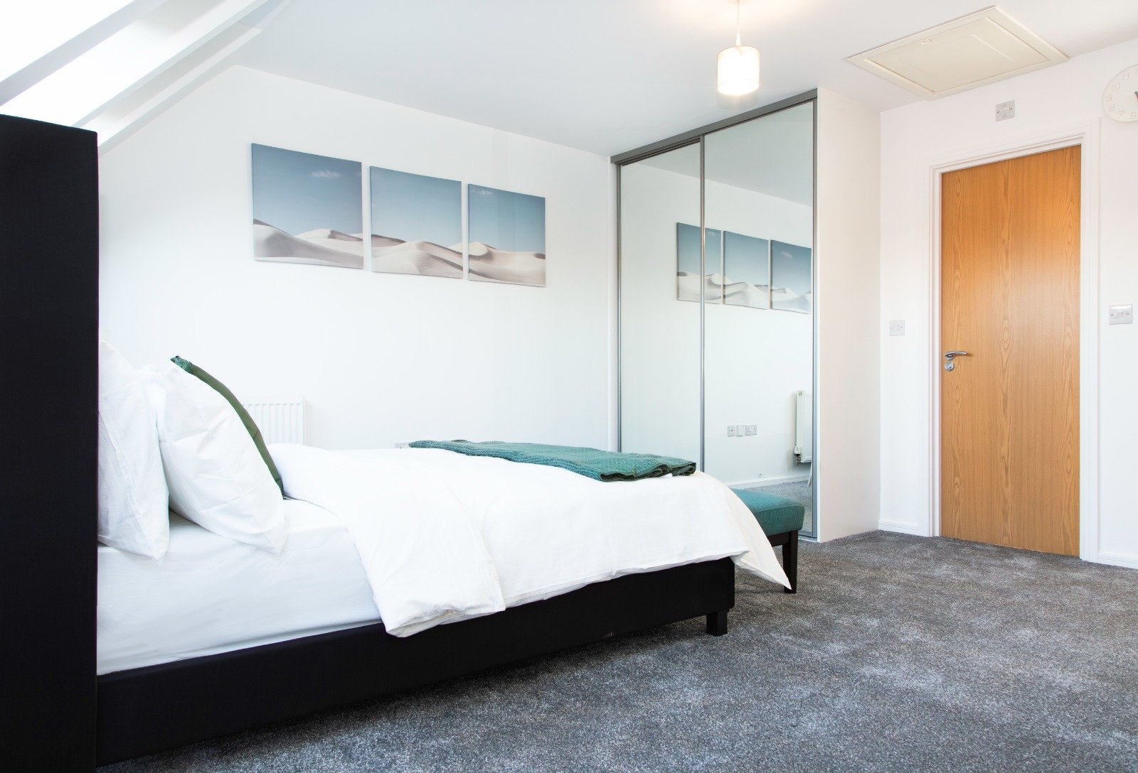 Modern bedroom with black bed frame, white bedding, mirrored wardrobe and wooden door