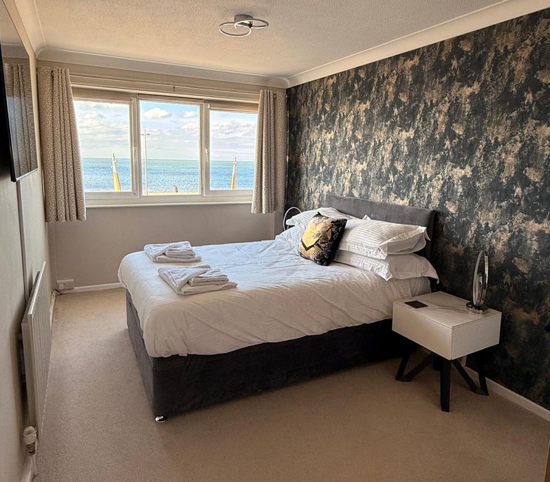 Bright bedroom with double bed, sea view windows, patterned wallpaper and bedside table