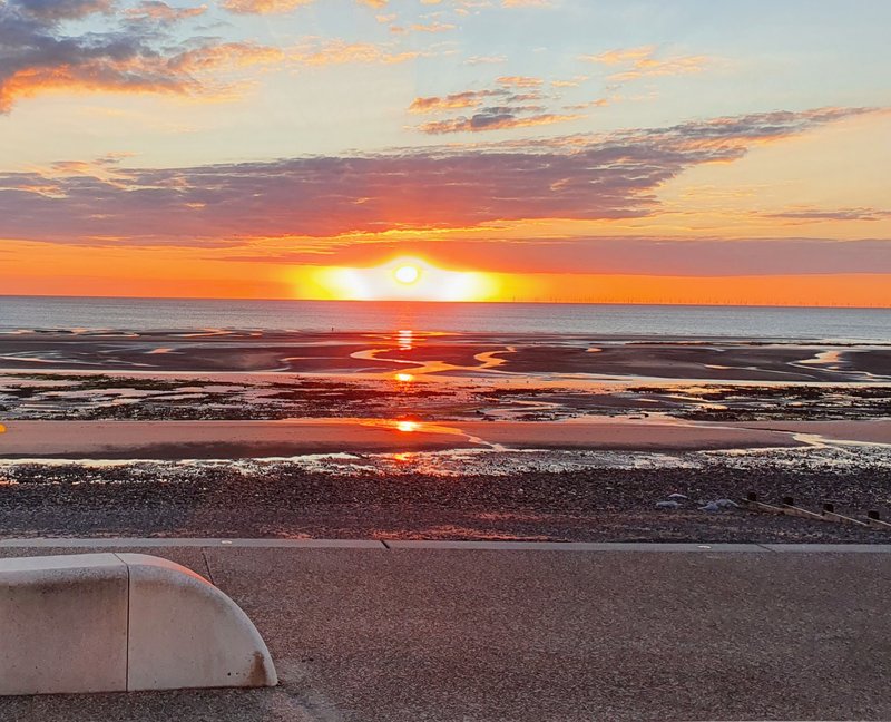 Sunset over the sea with golden and orange sky, waves and sandy beach in foreground
