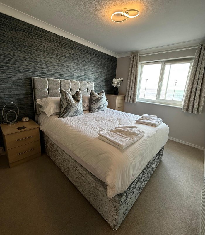 Modern bedroom with double bed, grey upholstered headboard, wooden nightstand, and large window