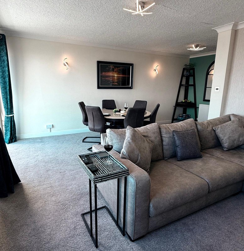 Open-plan living and dining area with grey sofa, dining table, chairs and wall-mounted TV