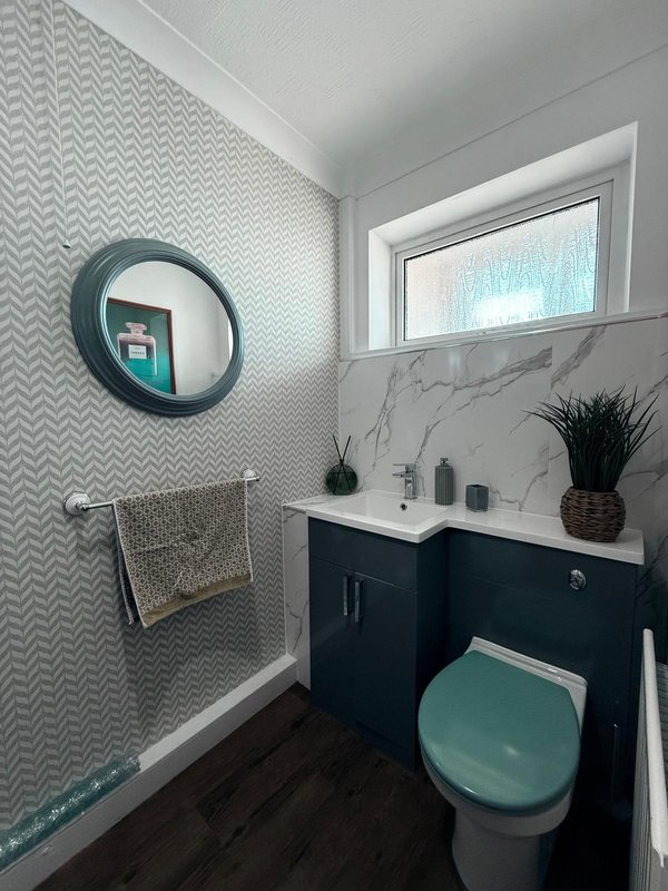 Modern bathroom with teal toilet, dark vanity, circular mirror and geometric tile walls