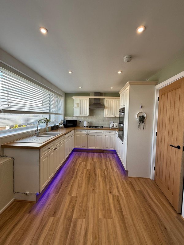 Modern kitchen with cream cabinets, wooden flooring, purple accent lighting and window over sink