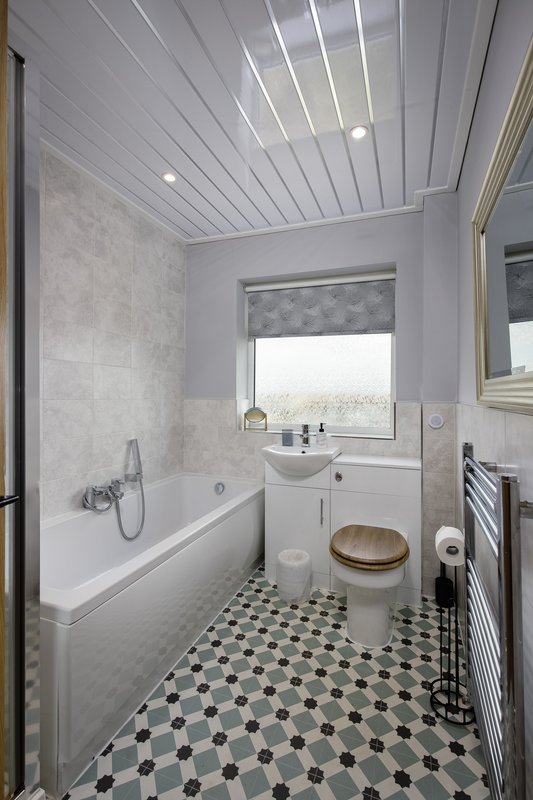 Modern bathroom with white panelled ceiling, bathtub, pedestal sink, black and white tile floor