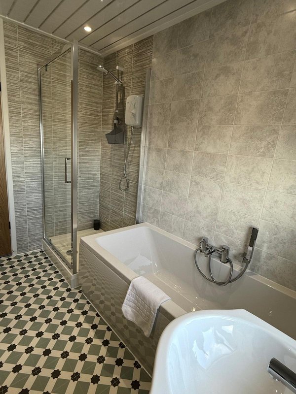 Modern bathroom with walk-in shower, white bathtub, geometric floor tiles and grey tile walls