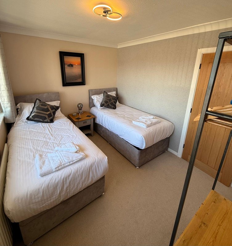 Twin bedroom with two single beds, wooden nightstand, framed artwork, and ceiling light fixture